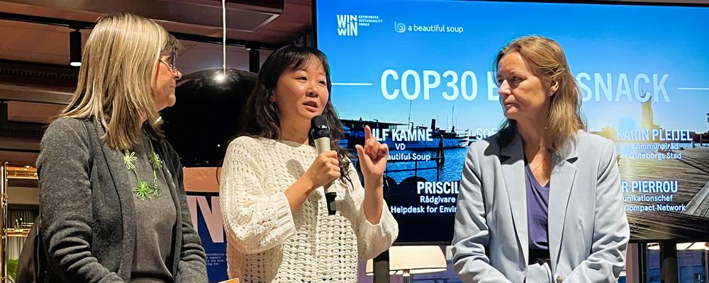Three women in a panel on a stage. One women holds a microphone and speeks.