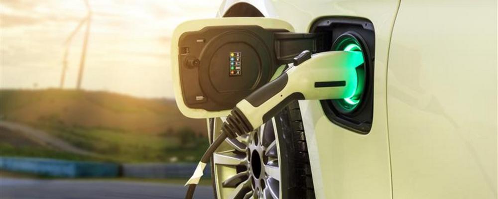 En elbil laddas med vindkraftverk i bakgrunden