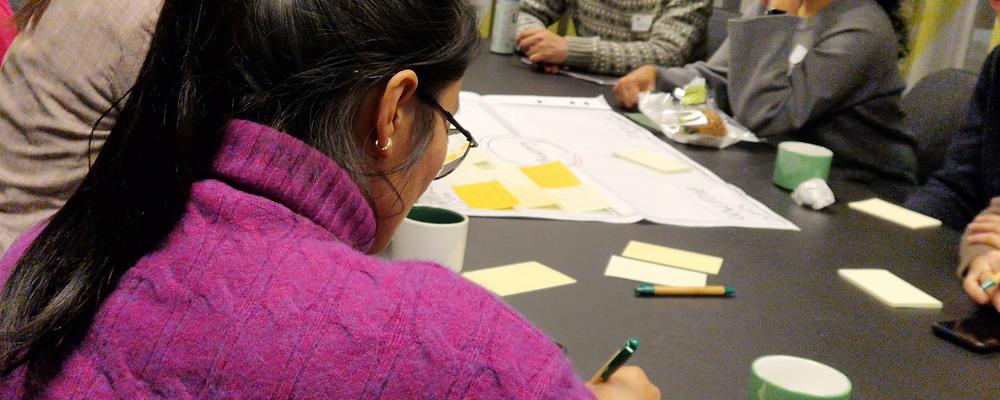 Unga män och kvinnor sitter med papper och penna runt ett bord