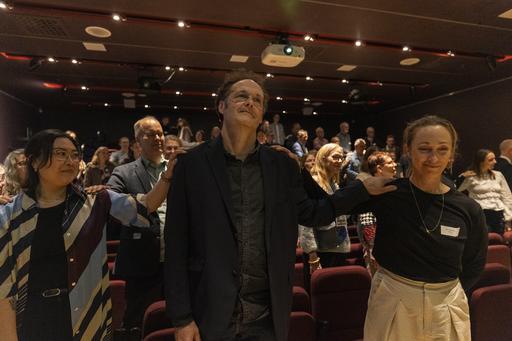 En stor grupp människor skapar band mellan sig genom att lägga handen på en annans axel.