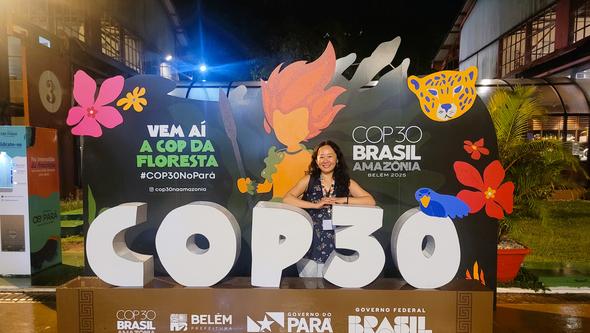 A woman standing by a sign that says COP30.